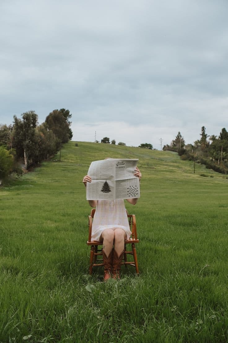 Alguien leyendo el periódico sentado en una silla en mitad del campo